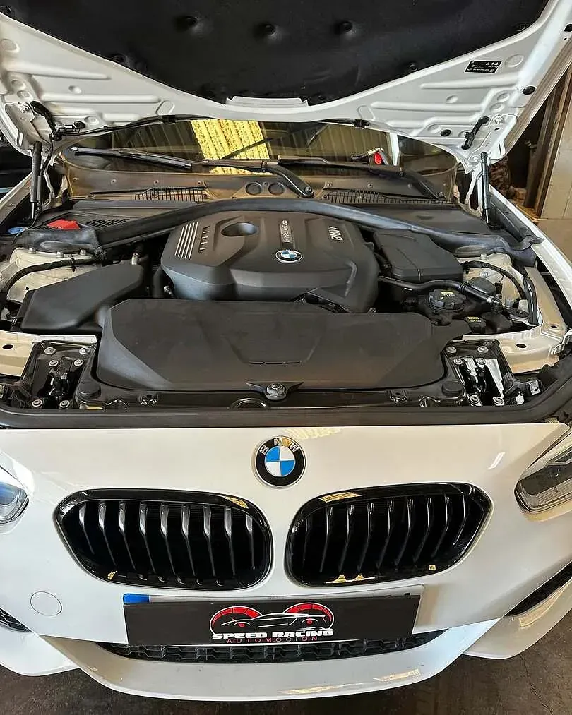 Se muestra el motor de un BMW blanco con el capó abierto.