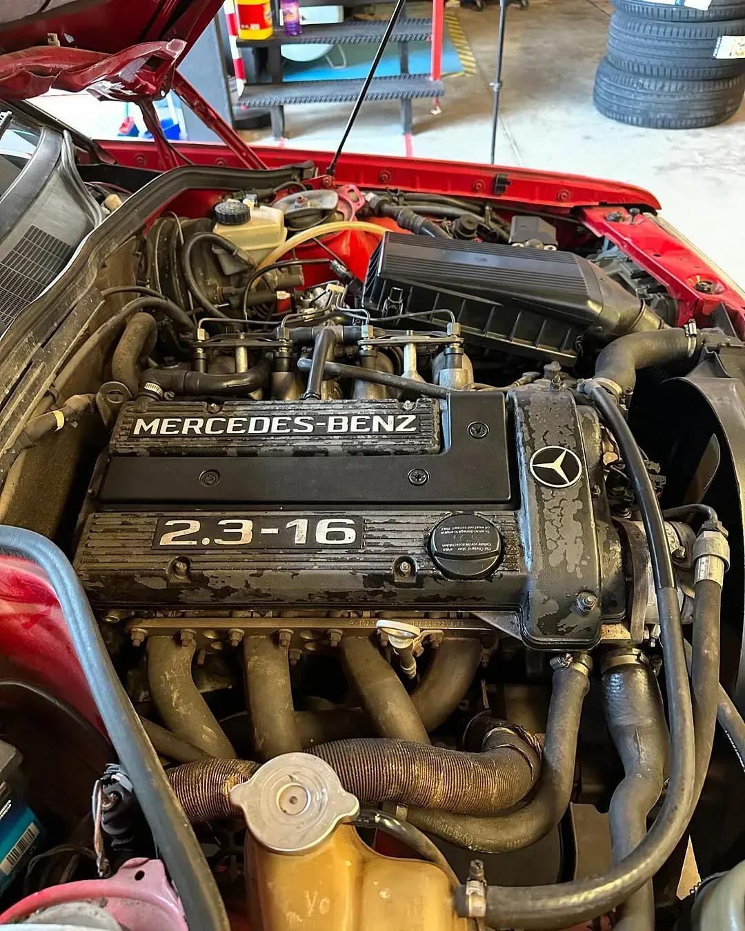 Se muestra el motor de un Mercedes Benz rojo con el capó abierto.