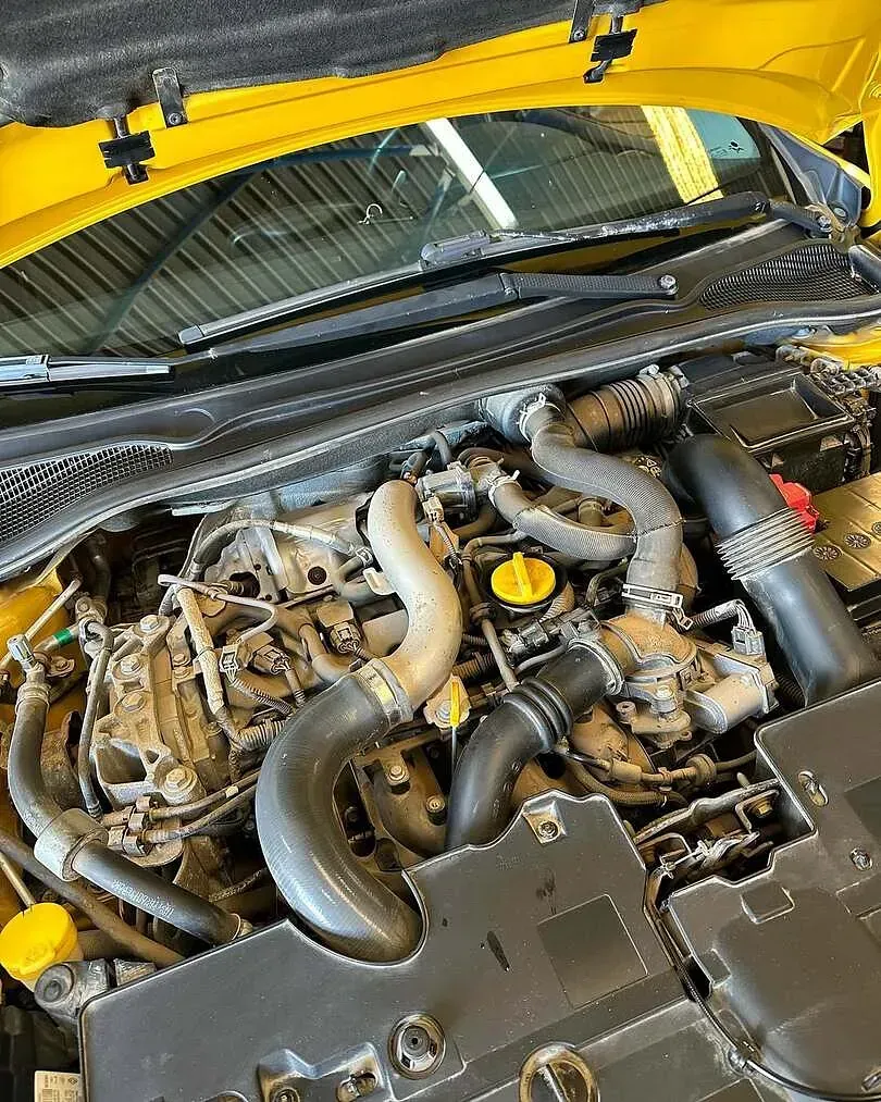 Se muestra el motor de un coche amarillo con el capó abierto.