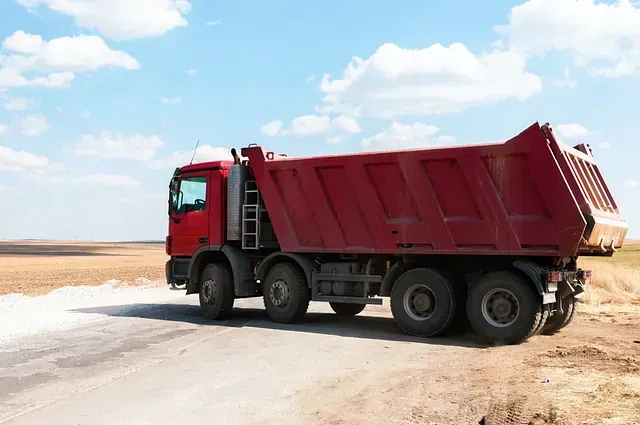 Un camión volquete rojo circula por un camino de tierra.