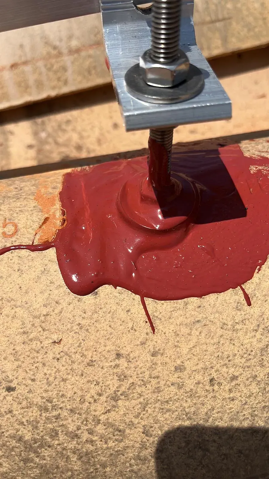 Un primer plano de un líquido rojo que sale de un tornillo en un trozo de madera.