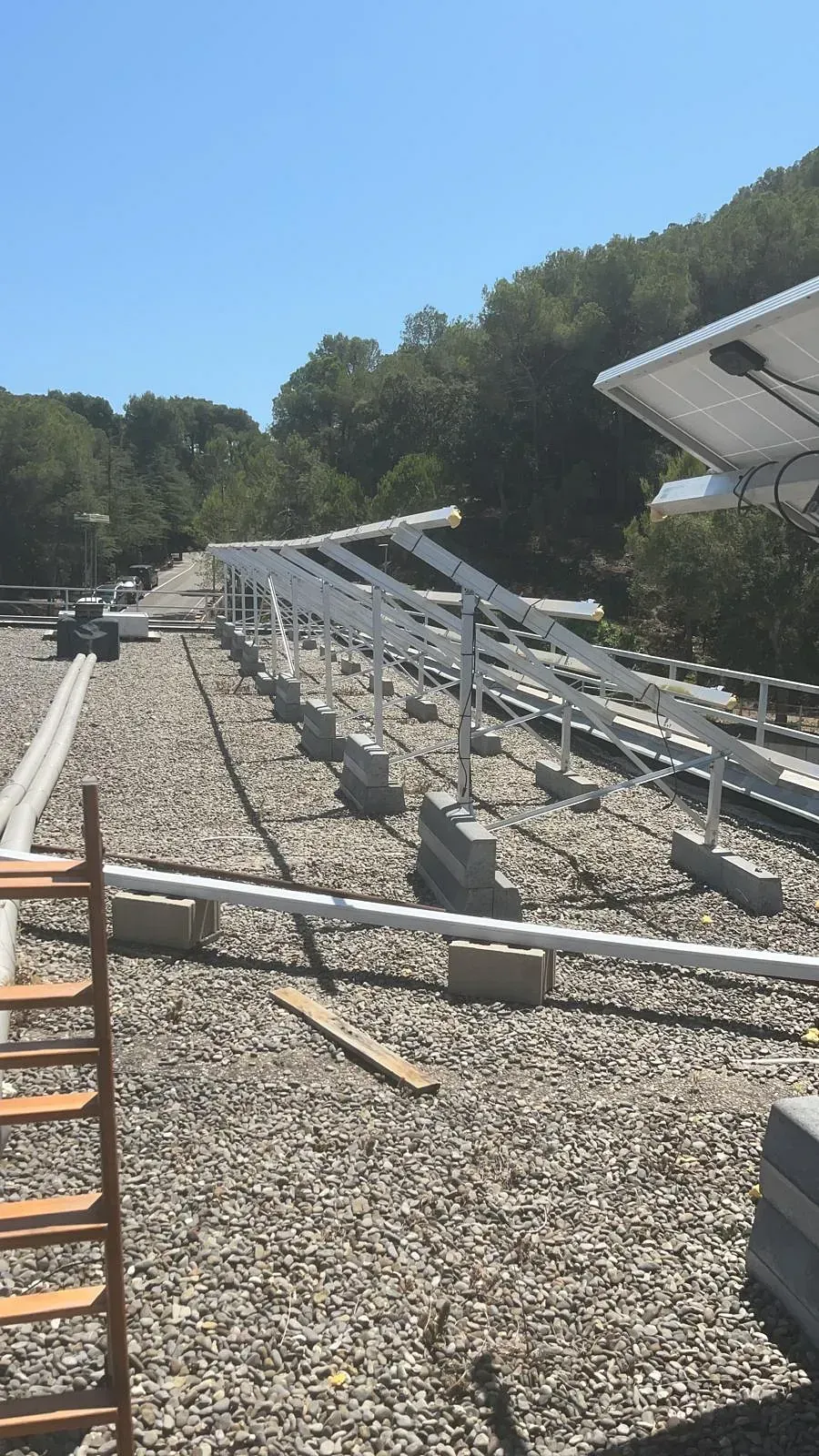 Una escalera está colocada encima de un techo de grava al lado de una fila de paneles solares.