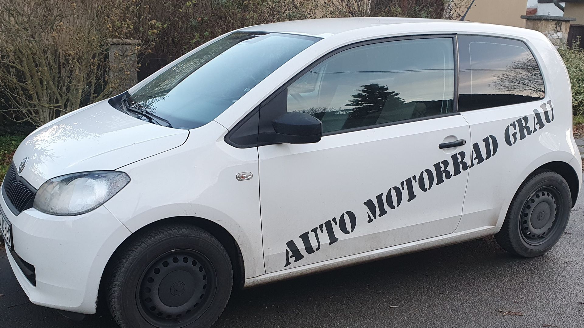 Nahaufnahme des Scheinwerfers eines blauen Autos in einem Autohaus, im Hintergrund ist ein anderes Auto verschwommen zu sehen.