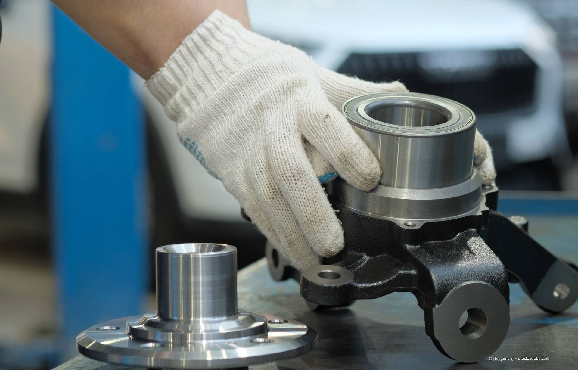 Die behandschuhte Hand eines Mechanikers hält eine Radnabenbaugruppe und eine separate Radnabe auf einer Werkbank in einer Reparaturwerkstatt.