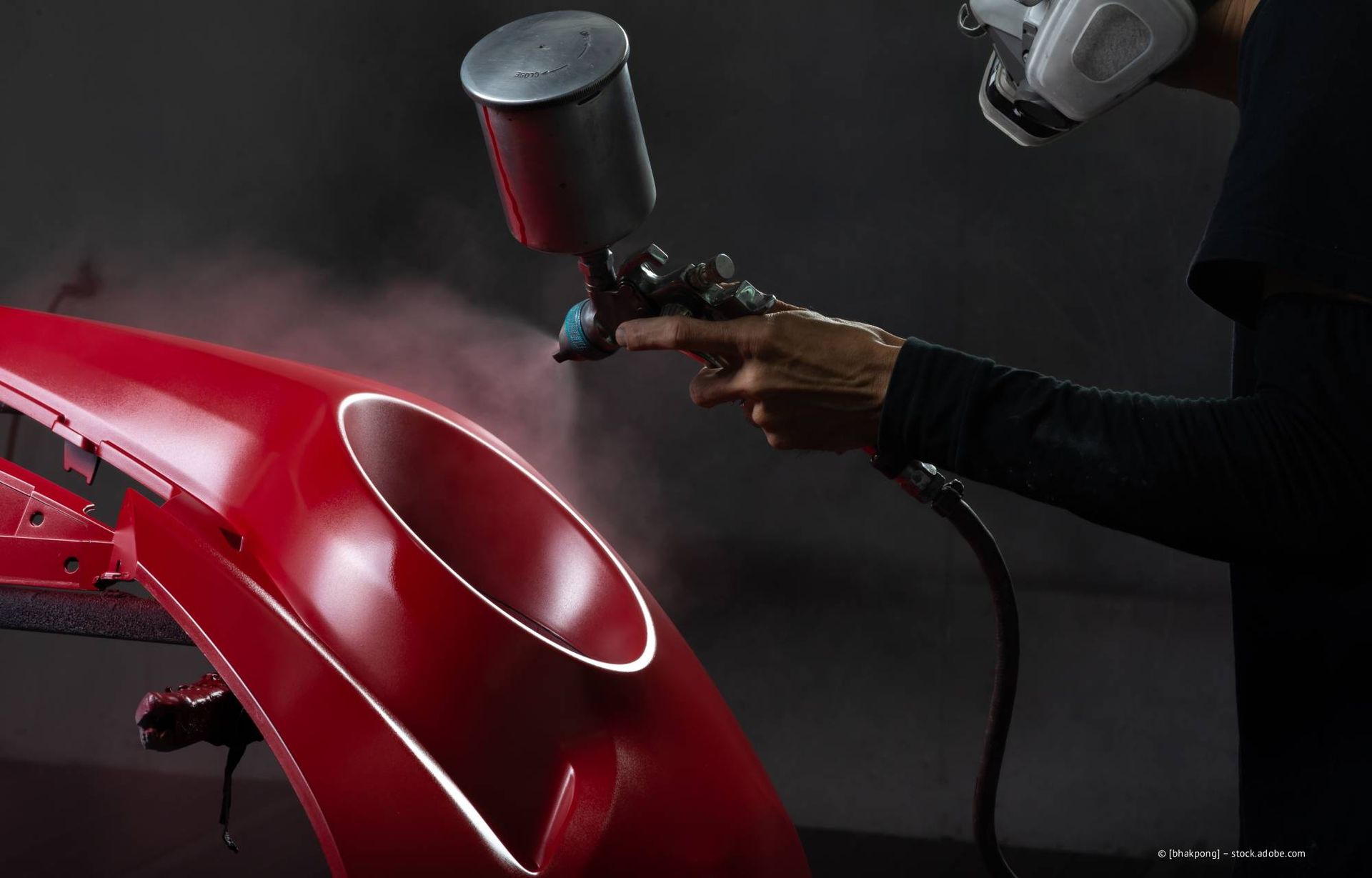 Eine Person besprüht ein Autoteil mit roter Farbe.