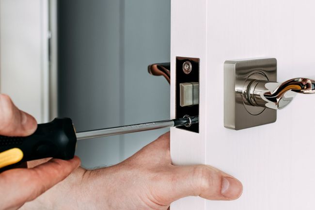 Una persona está arreglando una manija de puerta con un destornillador.