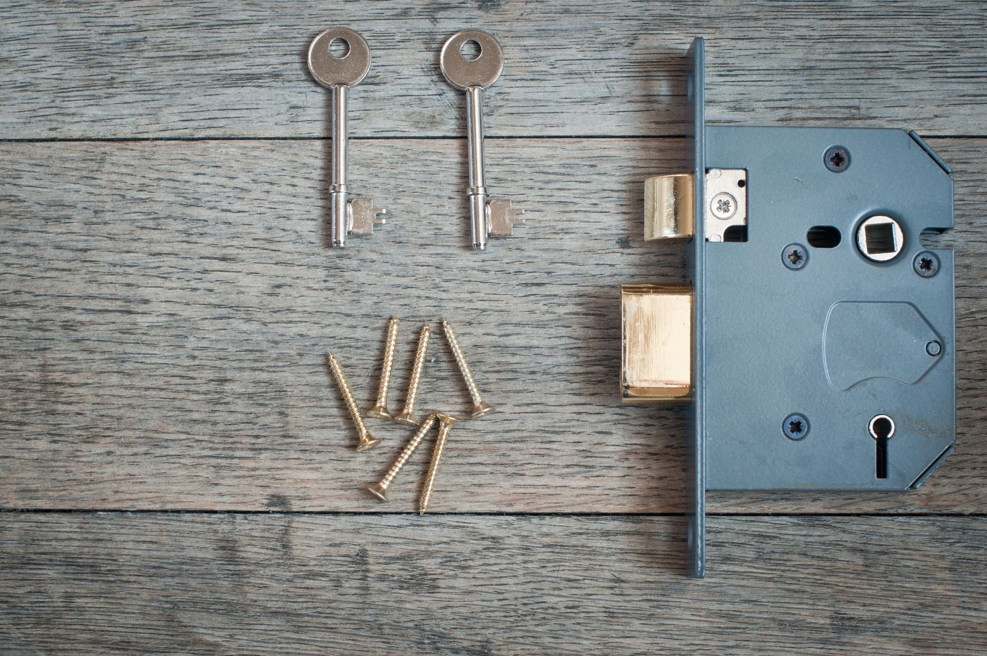 Una cerradura de puerta con llaves y tornillos sobre una mesa de madera.