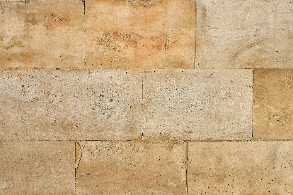 Bloques rectangulares de piedra de color tostado y beige forman una pared.
