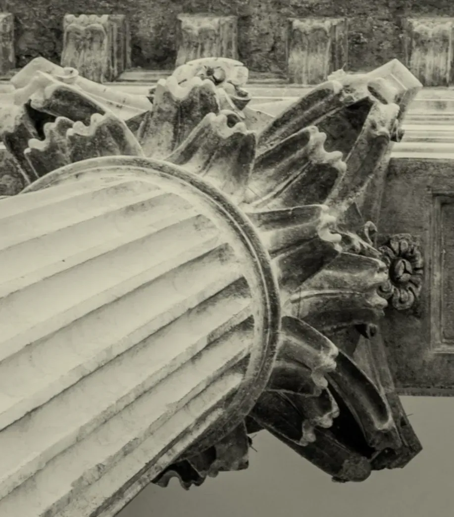 Primer plano de un capitel de columna estriado, con talla ornamentada y texturizada en tonos sepia.