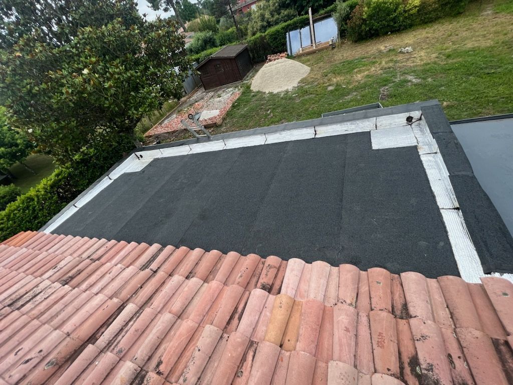 Toiture en tuiles rouges au premier plan, toit plat noir au second plan et jardin en arrière-plan.