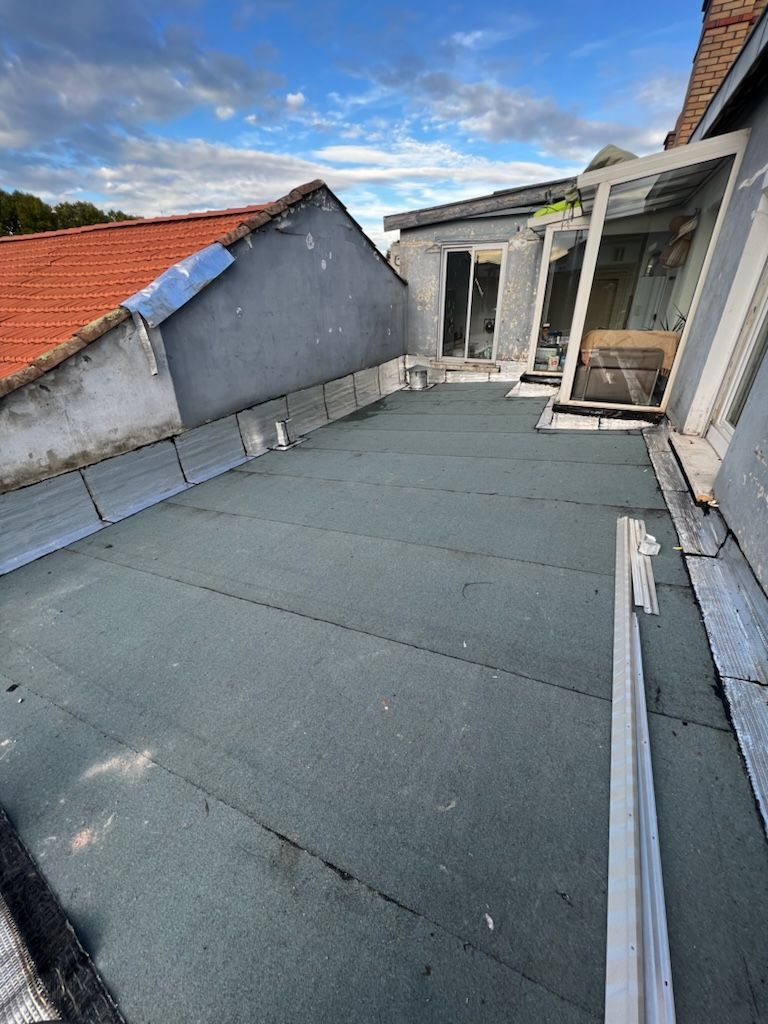 Toit plat à surface vert foncé se détachant sur un ciel bleu, relié au bâtiment.