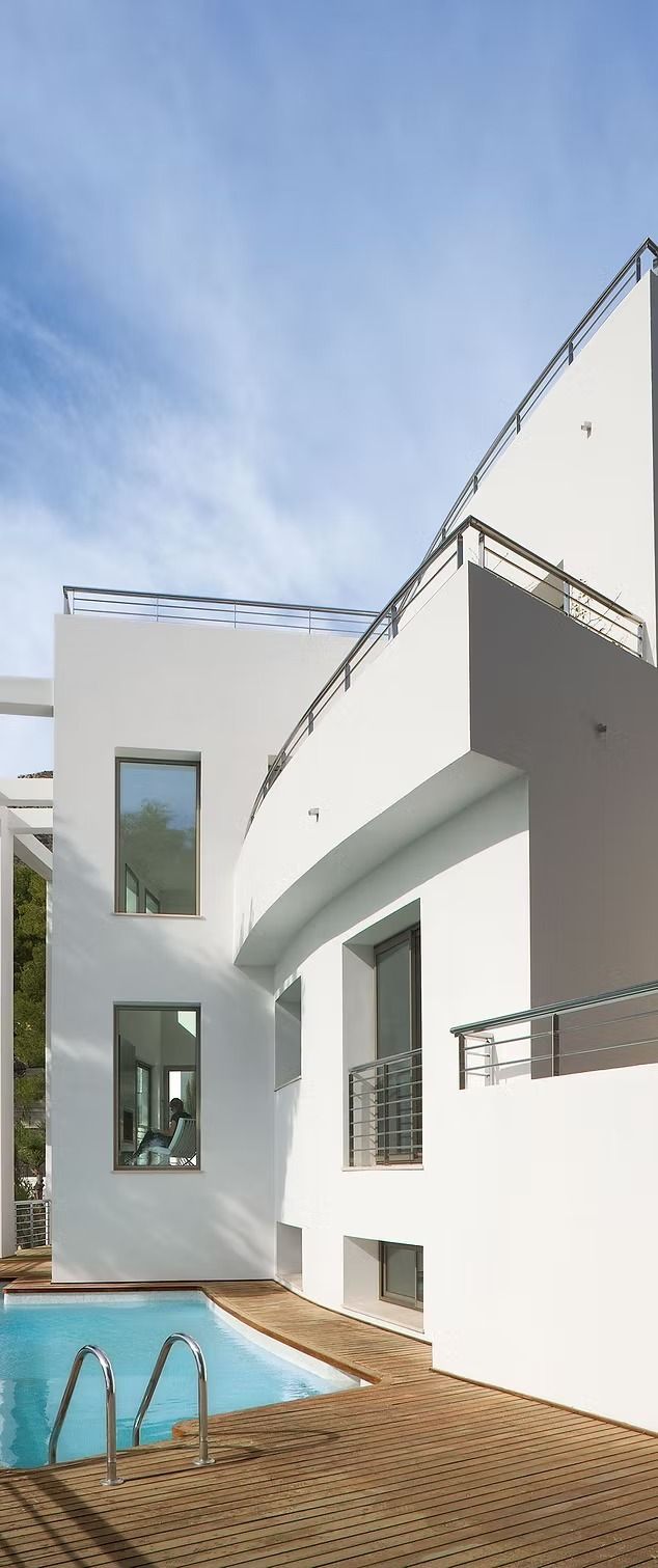 Casa blanca moderna con piscina azul y patio de ladrillo bajo un cielo despejado.
