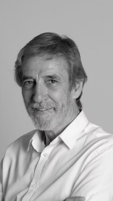Retrato de un hombre con camisa blanca, posando sobre un fondo gris liso, con una leve sonrisa.