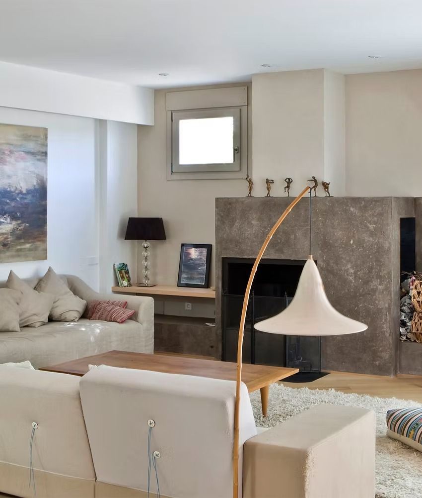Salón moderno con sofás beige, chimenea de piedra y lámpara de pie blanca.
