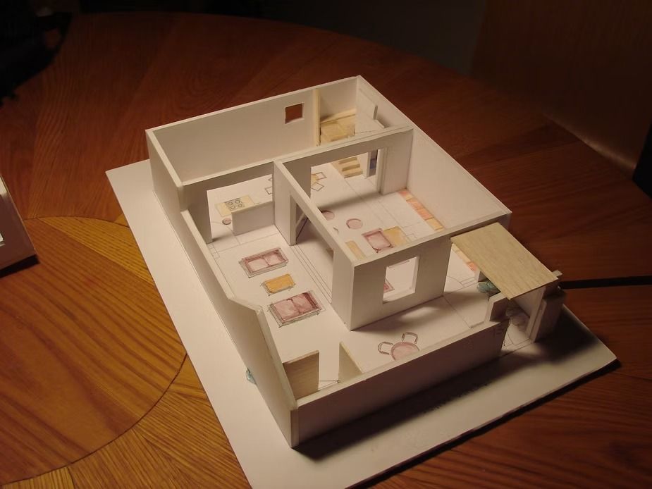 Maqueta de una casa blanca en miniatura sobre una mesa de madera, vista desde arriba con las habitaciones