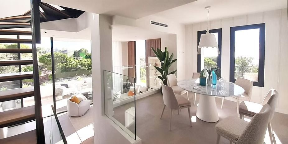 Comedor moderno y luminoso con mesa de cristal, sillas blancas y grandes ventanales que dan a un patio.