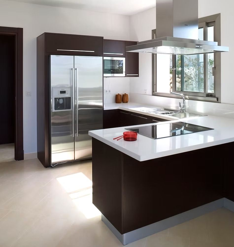 Cocina moderna con gabinetes oscuros, encimeras blancas, electrodomésticos de acero inoxidable 