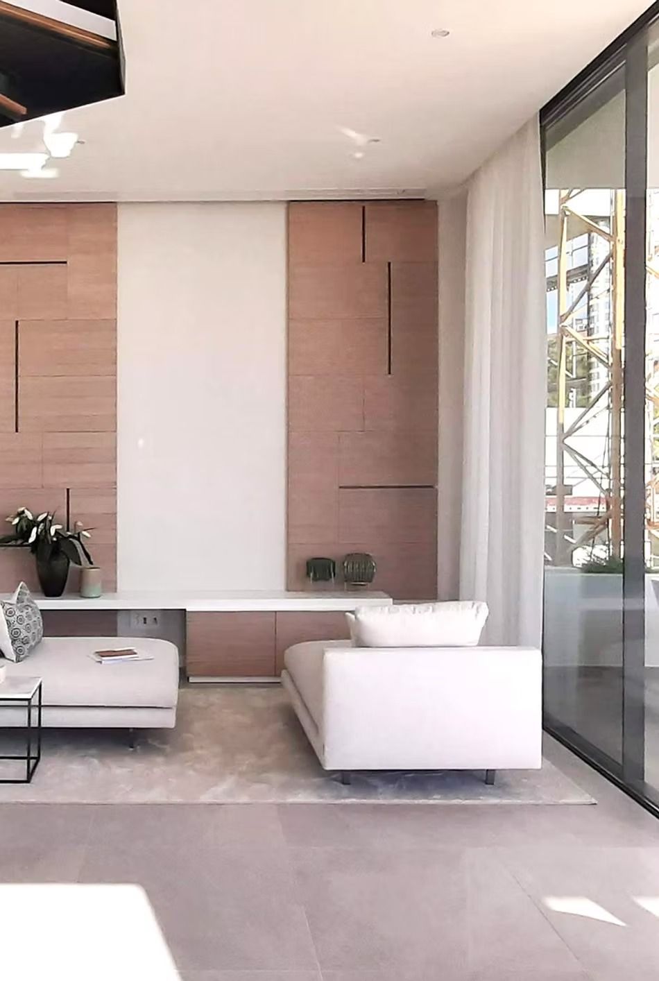 Sala de estar moderna con sofá blanco, paneles de madera beige y grandes puertas de cristal que dan a un patio.