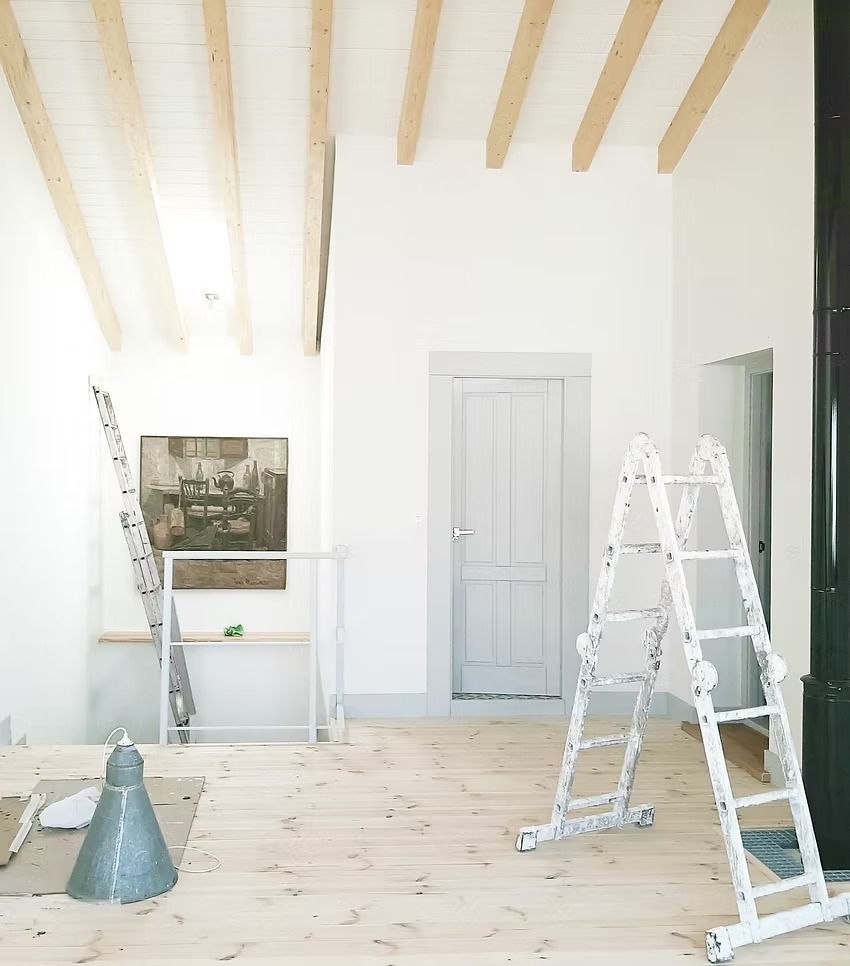 Habitación luminosa sin terminar con vigas de madera en el techo, paredes blancas