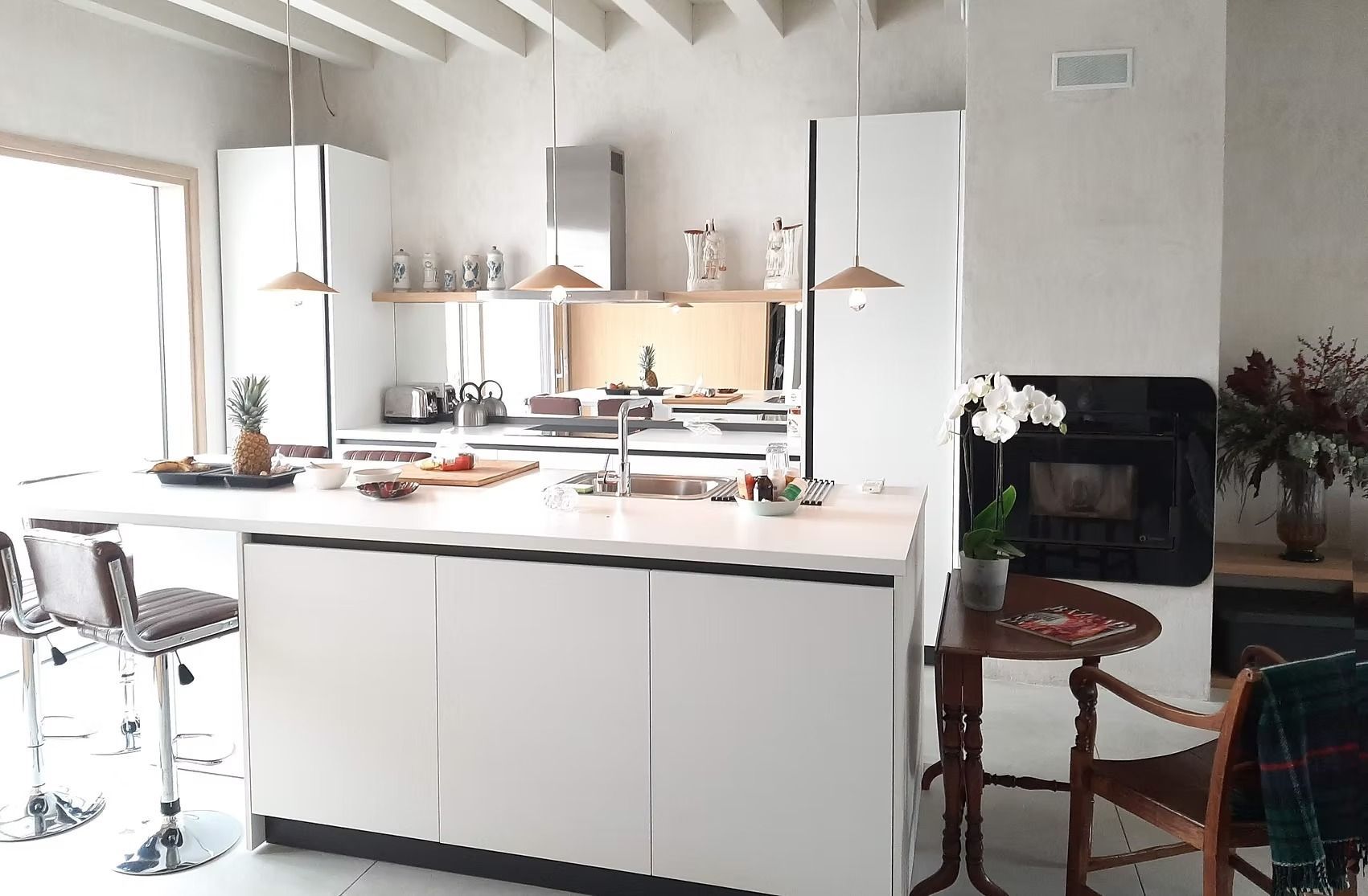 Cocina y comedor modernos de color blanco brillante con isla central, lámparas colgantes y sillas de madera.