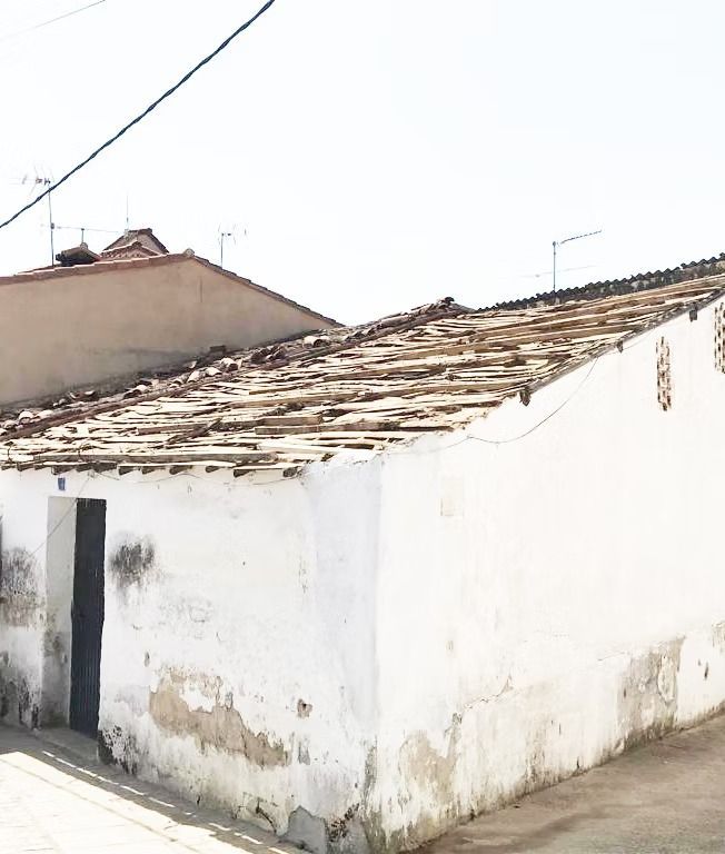 Antigua casa blanca con techo de tejas desgastado y paredes desconchadas en una esquina de la calle.