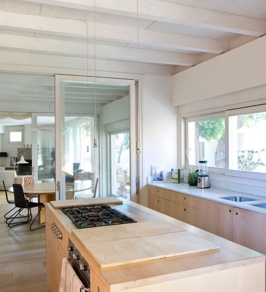 Cocina moderna y luminosa con una gran isla, placa de gas, armarios de madera y espejo que refleja el comedor.