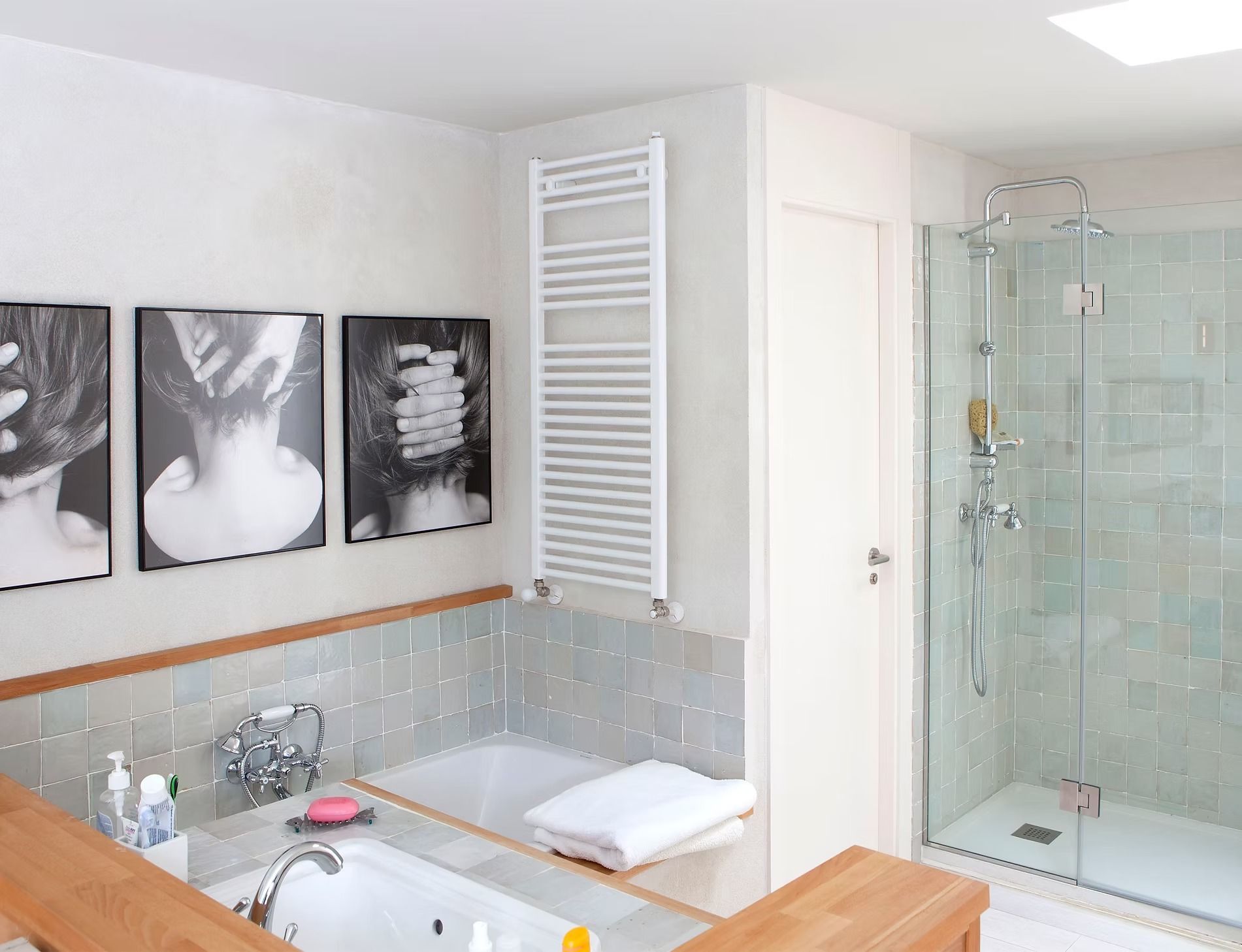 Baño moderno con bañera, ducha de cristal, azulejos blancos y cuadro en blanco y negro enmarcado.
