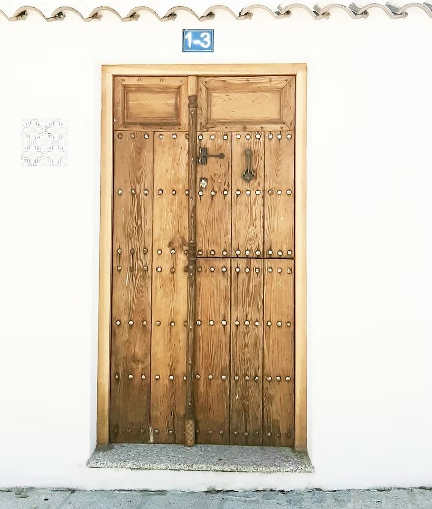Puerta doble de madera enmarcada en una pared de estuco blanco con el número 13 en azulejo encima.