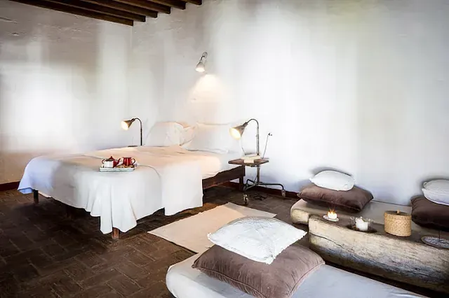 Dormitorio con ropa de cama blanca, una cama y dos sillones con almohadas.