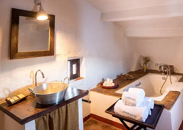 Baño con lavabo rústico, bañera, toallas y una pequeña ventana.