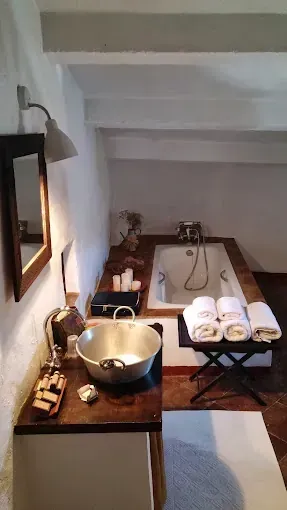 Baño con bañera, toallas, lavabo sobre encimera de madera y un pequeño taburete.