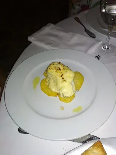 Plato blanco con rodajas de patata amarillas cubiertas con una salsa blanca cremosa.