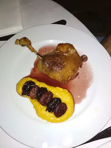 Confit de pato con polenta amarilla y cerezas en un plato blanco.