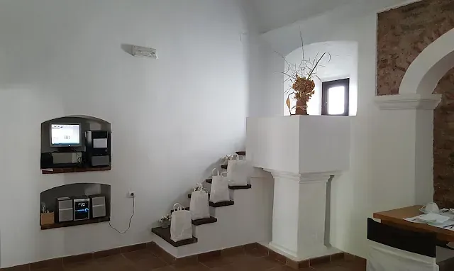 Interior blanco con escaleras incorporadas, pequeña ventana arqueada y estantes con dispositivos electrónicos.