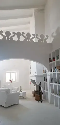 Un interior blanco y luminoso con una puerta arqueada, una barandilla ornamentada y estanterías empotradas llenas de artículos.