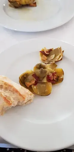Un plato blanco de comida que incluye pan y alcachofas con detalles rojos.