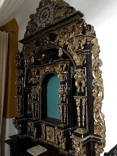 Marco elaborado de madera oscura con detalles dorados, una abertura verde arqueada y un reloj en la parte superior.