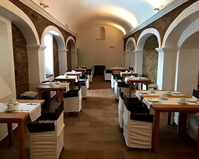 Comedor de restaurante con detalles de ladrillo arqueado, paredes blancas y mesas preparadas para una comida.