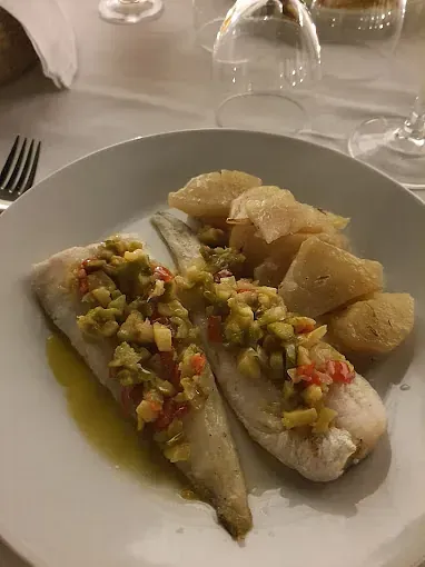 Dos filetes de pescado con una salsa colorida, servidos con patatas en un plato blanco.