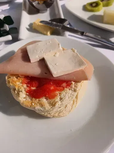 Un sándwich en un plato blanco: pan con tomate, jamón y cubitos de queso.