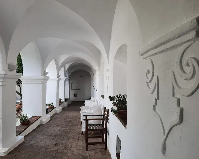 Pasillo arqueado blanco con sillas y plantas en macetas.