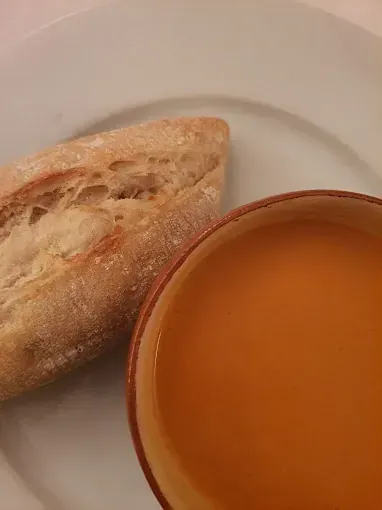 Tazón de sopa de naranja junto a una baguette de pan en un plato blanco.