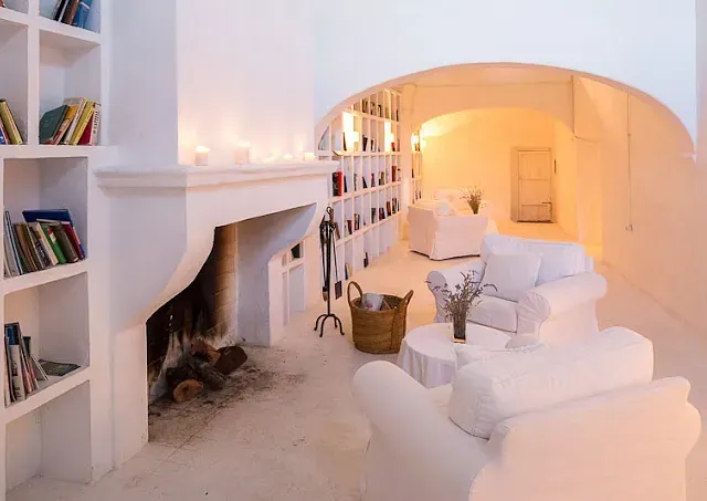 Sala de estar blanca con chimenea, estanterías empotradas y sofás blancos.