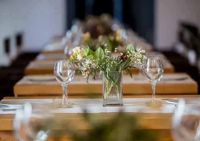 Largas mesas de madera dispuestas con flores, copas de vino y cubiertos.