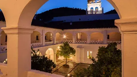 Patio con pasillos arqueados, árbol y edificio de noche.