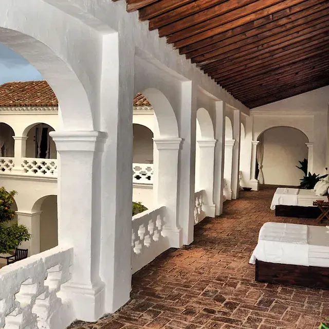 Pasillo abovedado blanco con piso de ladrillo, techo de tejas rojas y camas para descansar.