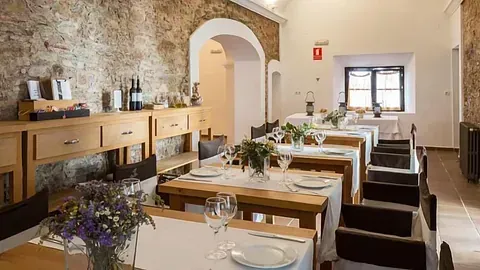Interior del restaurante: mesas de madera con mantelería blanca, paredes de piedra rústica, arreglos florales, iluminación suave.