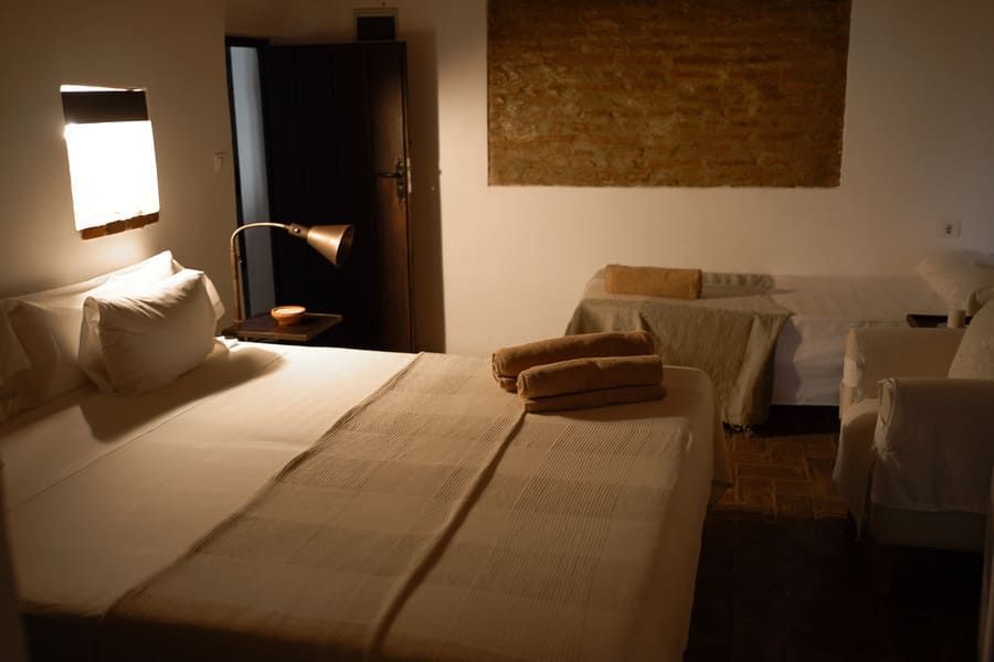 Dormitorio con cama, sofá pequeño y obras de arte. Tonos neutros e iluminación cálida.