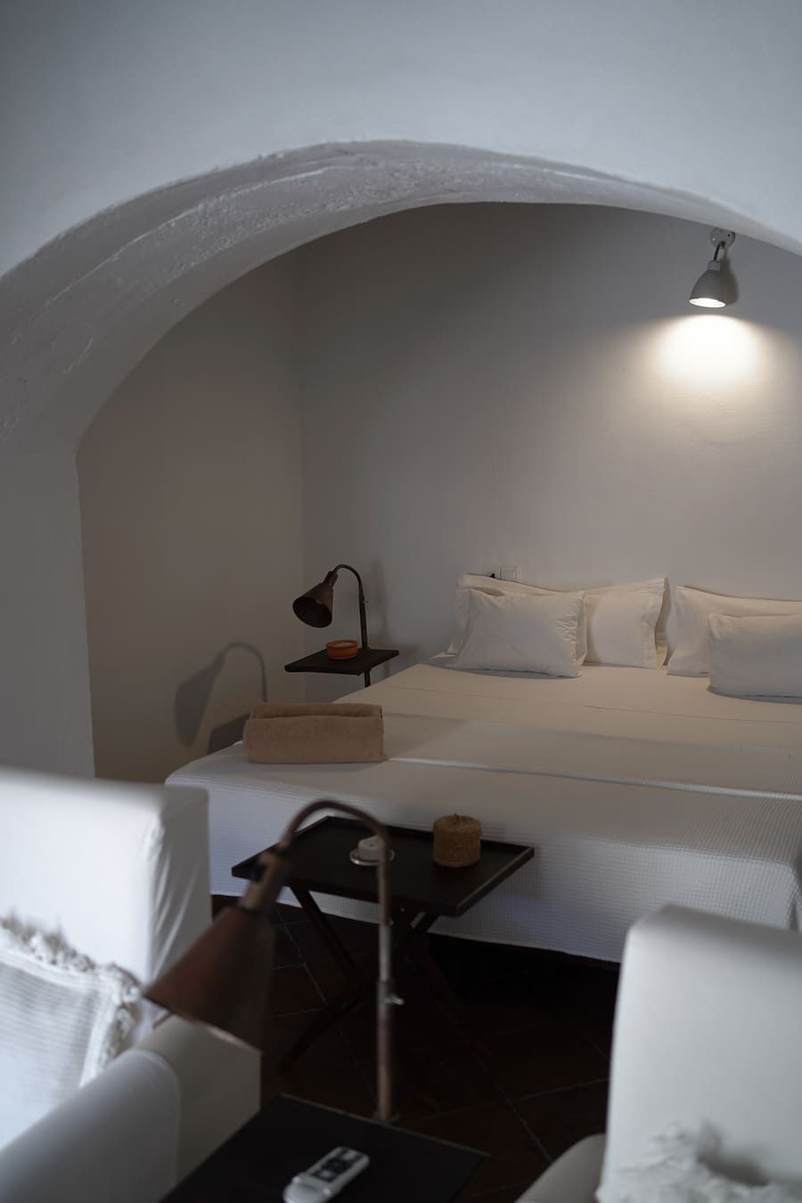 Acogedor dormitorio de paredes blancas con techo abovedado, cama, dos sillas y una pequeña mesa auxiliar.