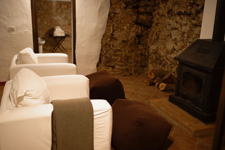 Acogedora zona de estar con sofás blancos, pufs marrones, chimenea y una pared de roca.